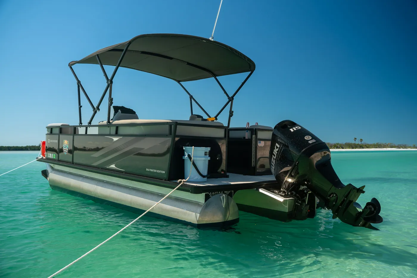 The pontoon boat anchored in clear turquoise water, seen from the stern quarter