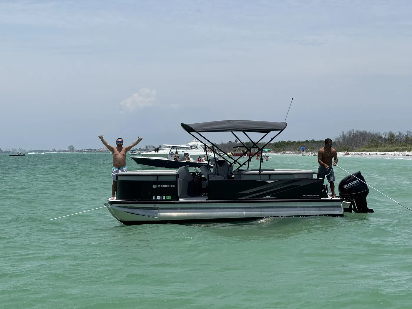 Two guests with arms raised aboard the pontoon anchored over shallow flats