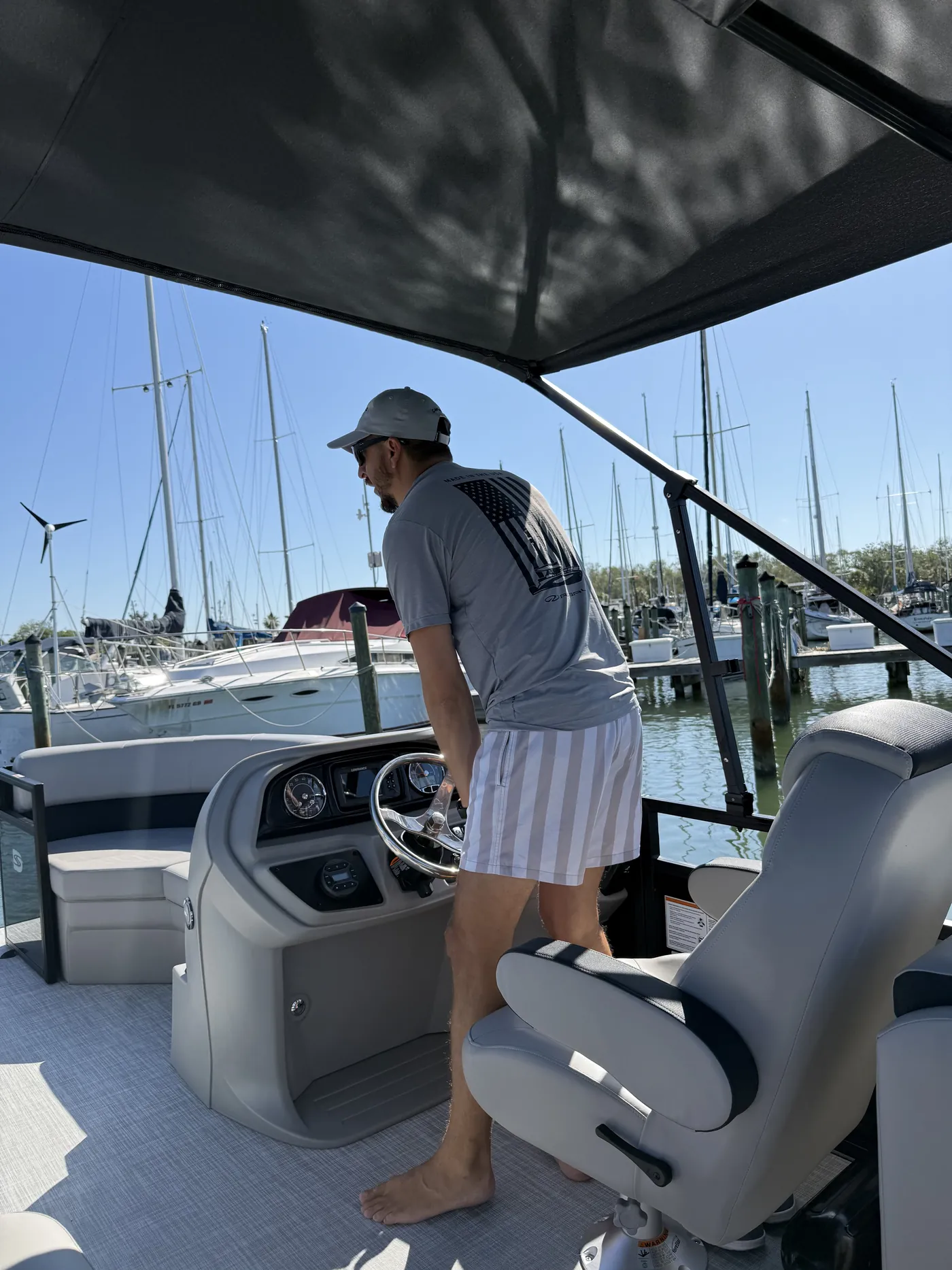 A guest standing at the helm of the pontoon under the bimini top leaving the Gulfport marina