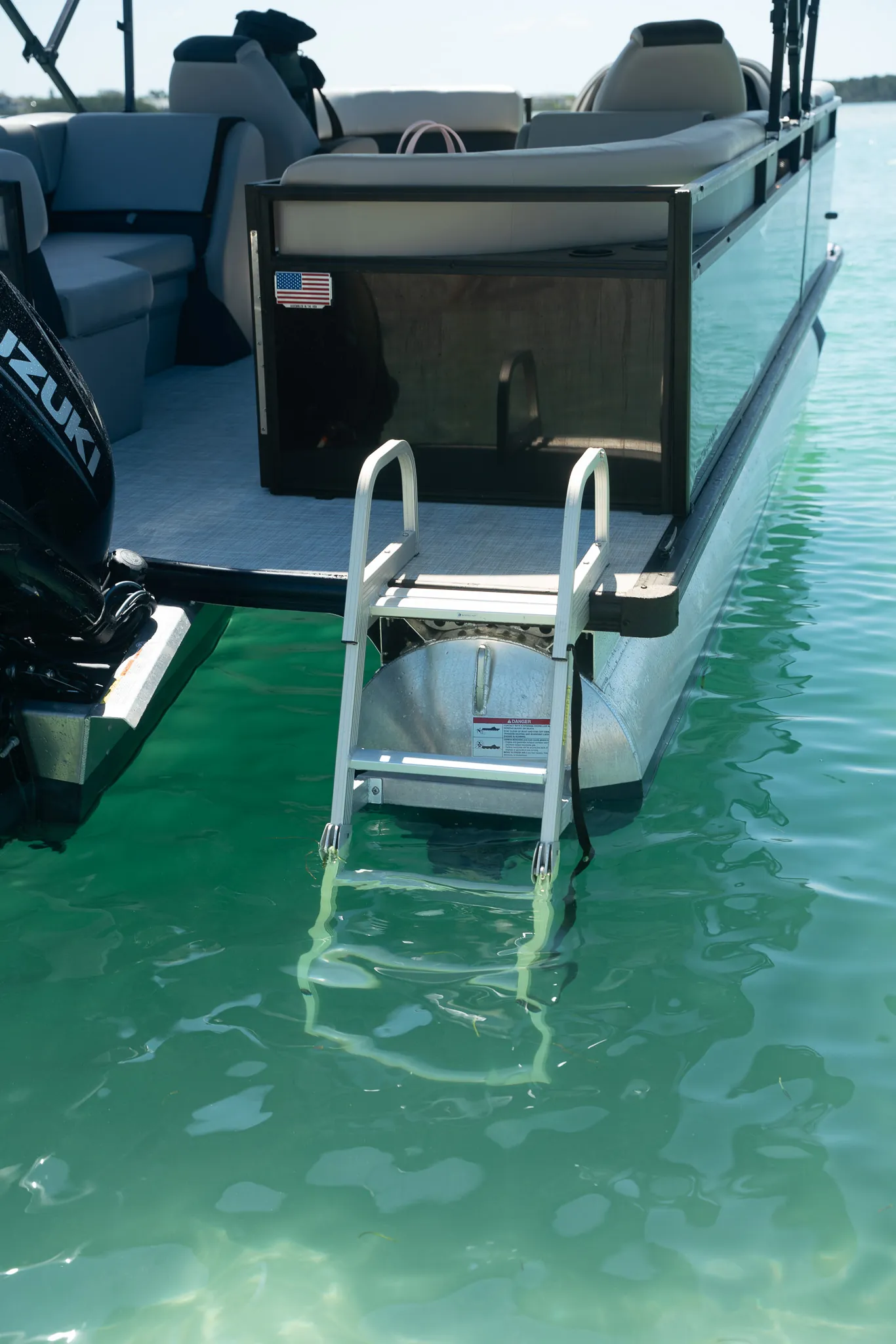 The rear boarding ladder and Suzuki outboard of the pontoon over clear green water