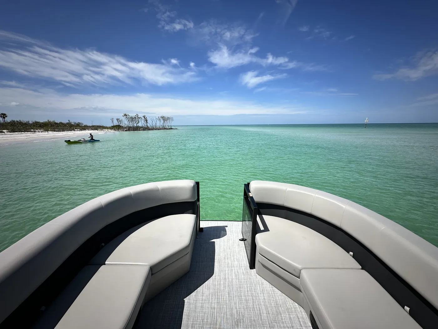 The pontoon bow lounge seating with a white sand beach and calm green water ahead