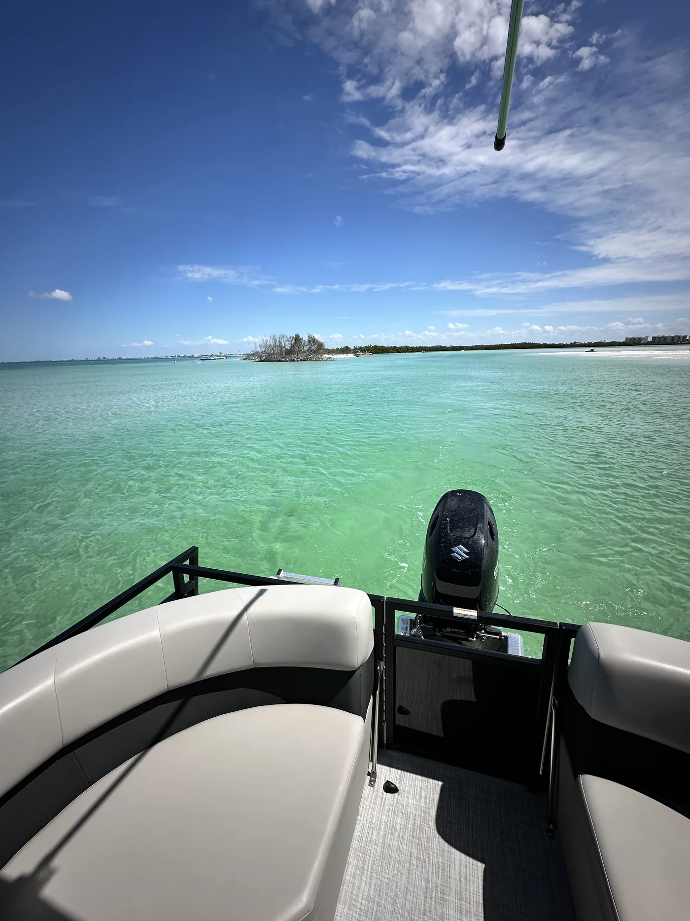 View from the bow seating of the pontoon looking across turquoise water toward a key