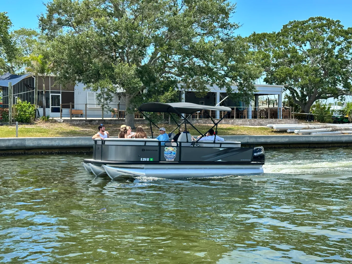 The pontoon cruising past waterfront homes and oaks on a sheltered canal near Gulfport