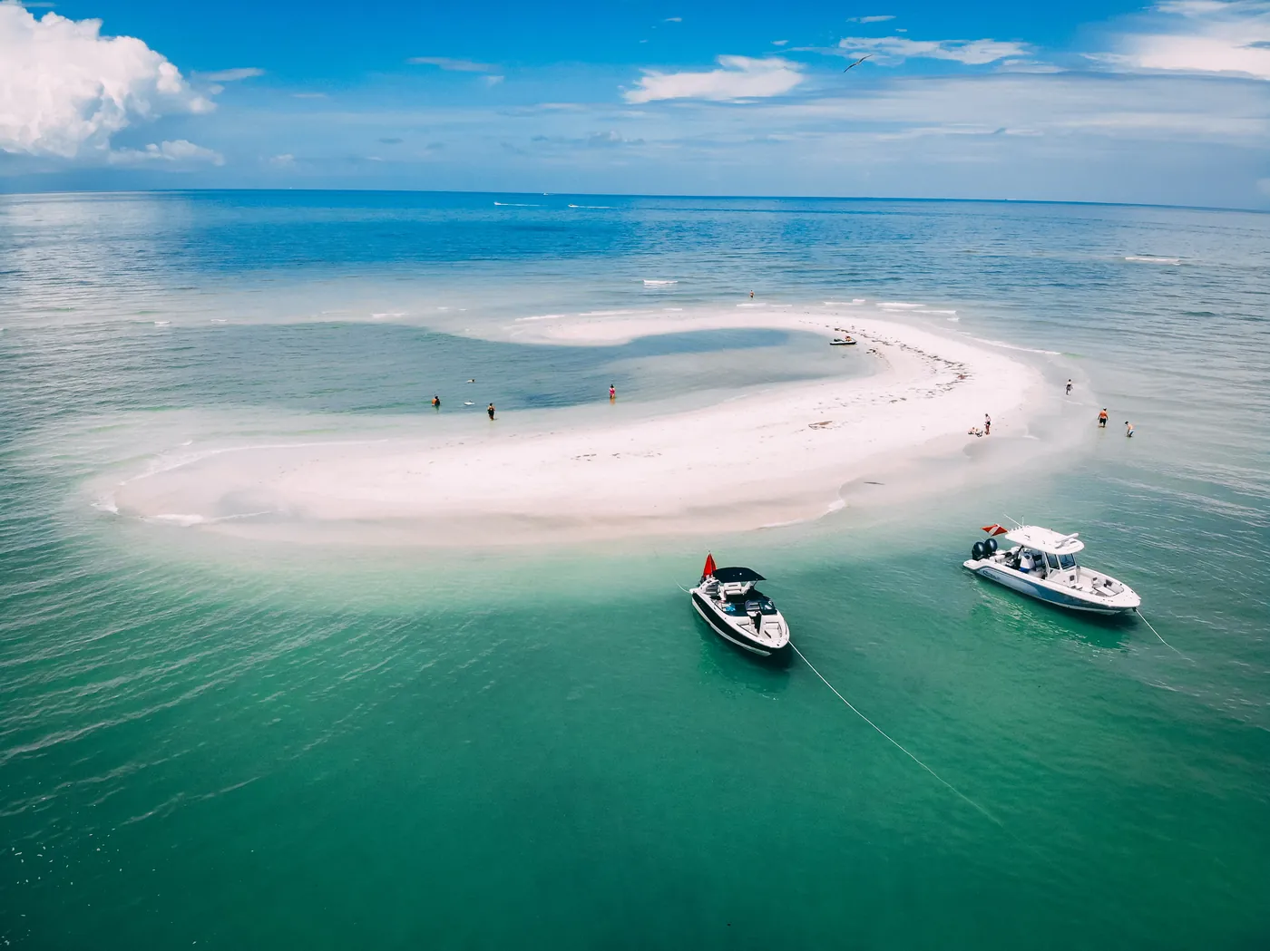 Aerial view of boats anchored along a curving white sandbar in shallow Gulf water