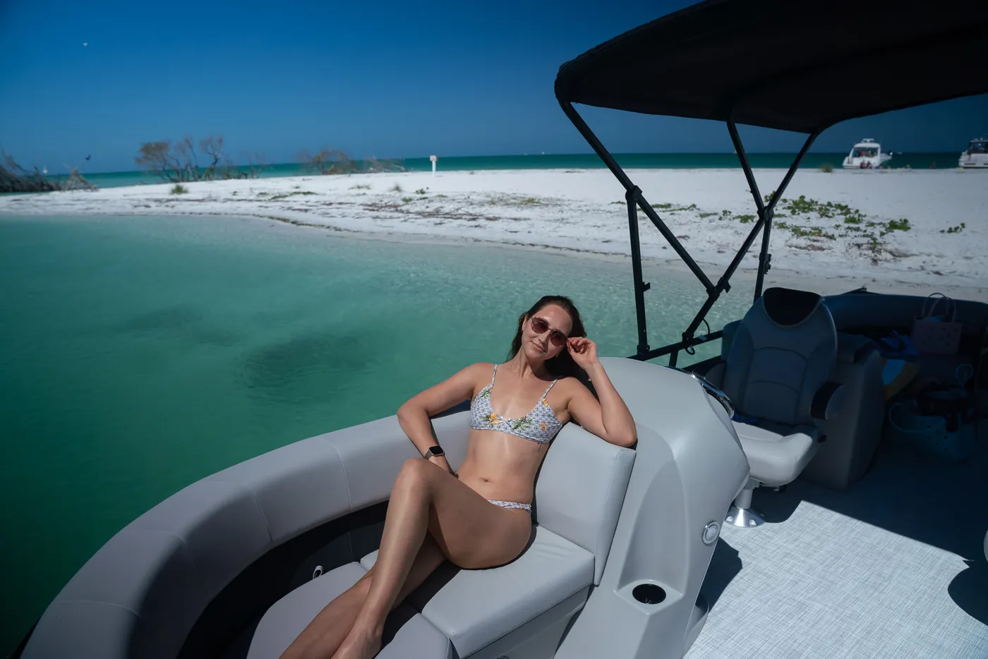A guest stretched out on the bow lounge of the pontoon with a white sandbar behind